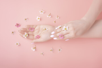 Obraz na płótnie Canvas Beautiful woman hands and flowers lie on a pink background. Natural organic cosmetic care concept template mockup