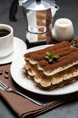Classic tiramisu dessert on ceramic plate, milk or cream and cup of coffee on concrete background