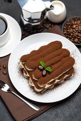 Classic tiramisu dessert on ceramic plate, milk or cream and cup of coffee on concrete background