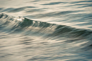 Abstract, blurred small Pacific ocean wave breaking at sunset