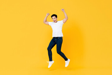 Happy young Asian man jumping with hands up isolated on yellow background