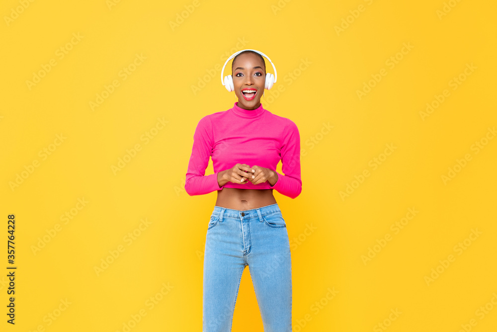 Wall mural fashionable african american woman with headphones smiling on colorful yellow isolated studio backgr