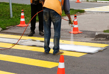 road workers create a new pedestrian crossing spray white paint on a stencil