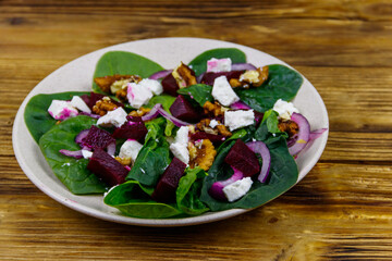 Tasty spinach salad with boiled beetroot, feta cheese, walnut and red onion on wooden table. Healthy vegetarian food