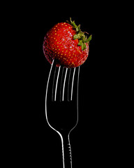 red strawberries on a fork, close-up isolated on a black background