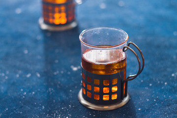 Orange homemade tea in transparent glass metal cup on the trendy concrete phantom blue cosmos...