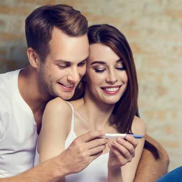 Happy amazed couple, finding out results of a pregnancy test, against loft style wall. Love, relationship, dating, happy lovers concept picture. Square composition.