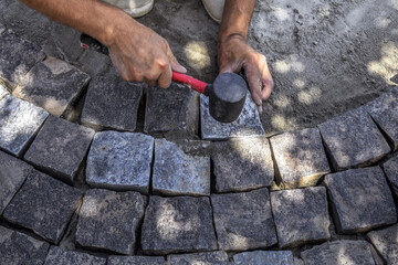 The installation process of gray granite stones during the repair of the sidewalk, top view. Man(s) hands tap with a mallet on gray square blocks, construction background with copy space