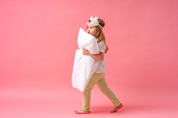 cheerful little girl in a sleep mask looks out from behind a pillow