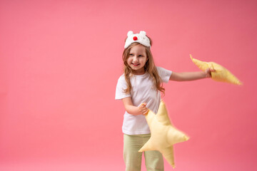 An adorable little girl in a sleep mask and pyjamas is holding pillows
