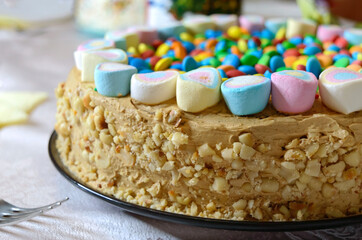 Beautiful caramel nut cake decorated with colorful marshmallows and sweets on the festive table.