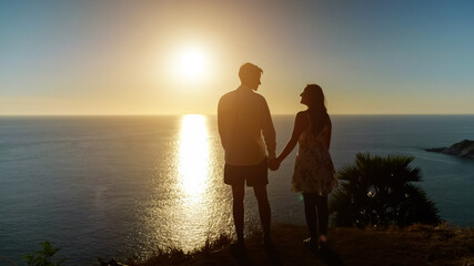 couple holding hands goes to viewpoint edge at wonderful sunset reflecting in ocean