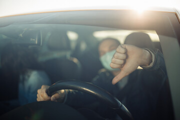 Taxi driver shows dislike thumb down wearing sterile medical mask holds hands on the steering wheel...