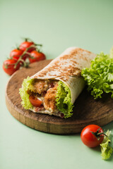 Fototapeta na wymiar Roll with chicken and fresh cherry tomatoes and lettuce on a wooden Board on a bright green background.