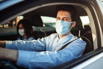 Young boy taxi driver gives passenger a ride wearing sterile medical mask. A man in the car behind the steering wheel works during coronavirus pandemic. Social distance and health safety concept.