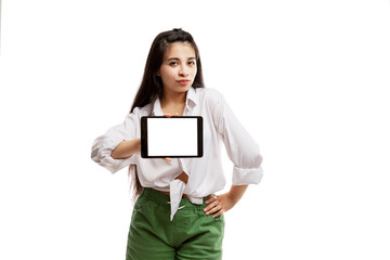 Fototapeta premium Serious young girl in a white shirt and green shorts shows a blank white screen tablet. Brunette with long hair. Isolated on a white background. Space for text.