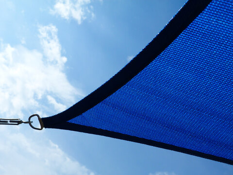 weaved breathing blue fabric sun shade material. patio awning. spanning over terrace. blue sky and white clouds. abstract low angle view. metal connector and chain. summer and outdoors concept.
