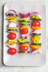 Cooking raw vegetable skewers on gray rectangular plate, top view. Vegan food concept.