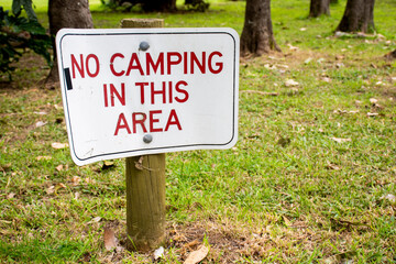No camping in this area sign on a green grass surrounded by trees.