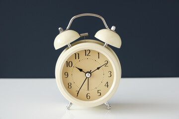 White vintage alarm clock on white surface and isolated on dark blue background.