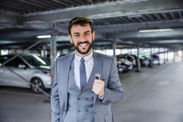 Fototapeta premium Young smiling handsome man in suit just bought a car and holding his keys.