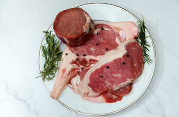 The mix of raw beefsteak tomahawk rib-eye tenderloin and strip loin with herb on marble background