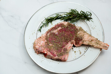 Raw Tomahawk steak with rosemary on a marble background