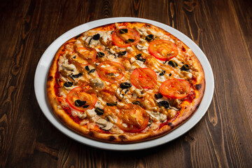 Pizza with chicken meat, mushrooms, tomatos and black olives, wooden background, low key