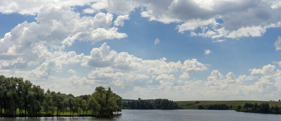 Panorama of the sky with cumulus clouds over the reservoir