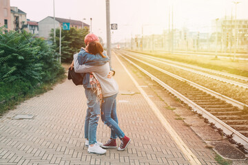 Female friends hugging railway platform saying goodbye - Two young millennials women affectionate meeting hugging train station