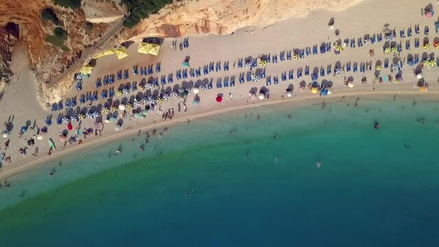 Neat rows of beach tents line an emerald green beach along the coast near Lefkada, Greece, aerial god view