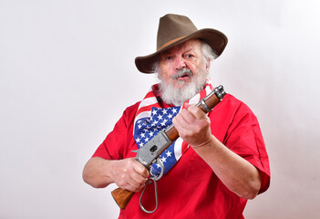 Determined looking old man with a sawed off rifle, wearing patriotic colors, and a floppy western hat..Unsociable man not giving a welcoming look.