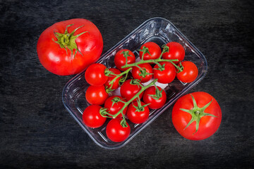 Cherry tomatoes in food container, ordinary tomatoes on black surface
