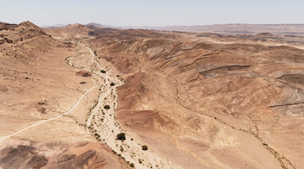 Fototapeta na wymiar aerial view of wadi gevanim dotted with acacia trees looking west with the desert town of mitzpe ramon on the cliff in the right far background