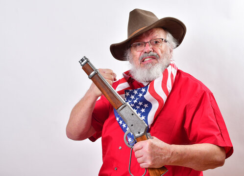 Angry old man, armed with a sawed off rifle, wearing patriotic colors, eyeglasses and a floppy western hat.