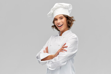 cooking, culinary and people concept - happy smiling female chef in toque with crossed arms over...