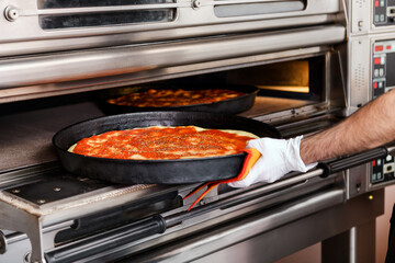 Chef placing a pizza on a tray into an oven