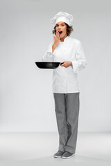 cooking, culinary and people concept - surprised female chef in toque with frying pan over grey background