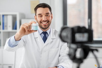 healthcare, medicine and blogging concept - happy smiling male doctor with camera showing drug and...