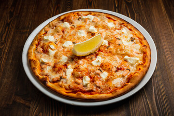 Fish and feta cheese pizza with a slice of lemon, wooden background, low key
