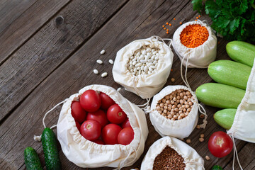 Textile grocery bags with groats and fresh vegetables on wooden table overhead. Meal donate or food supplies concept