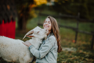 Portrait of teen girl hugging with a white goat in a farm. Copy space.
