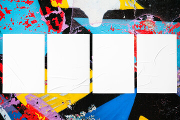 Closeup of colorful messy painted urban wall texture with four wrinkled glued poster templates. Modern mockup for design presentation with clipping path. Creative urban city background