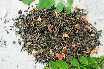 dried tea leaves with berries and fresh green leaves on a white cement background