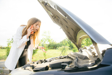 assistance on the road - worried woman standing in front of broken car, looking at engine and calling for help