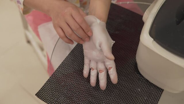 Woman removes paraffin wax from her hand after treatment and showing skin result