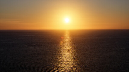 marvelous bright yellow sunlight reflected in calm endless ocean creating sun path under clear sky with orange disk in evening