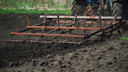 The tractor cultivates and cuts furrows in the field. Tractor work in the black soil field in the village