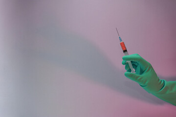 Beautiful hand holding creative syringe with red vaccine in the neon light. Minimalism retro style...