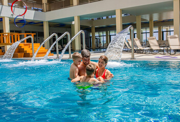 Smiling family of four having fun and relaxing in indoor swimming pool at hotel resort.